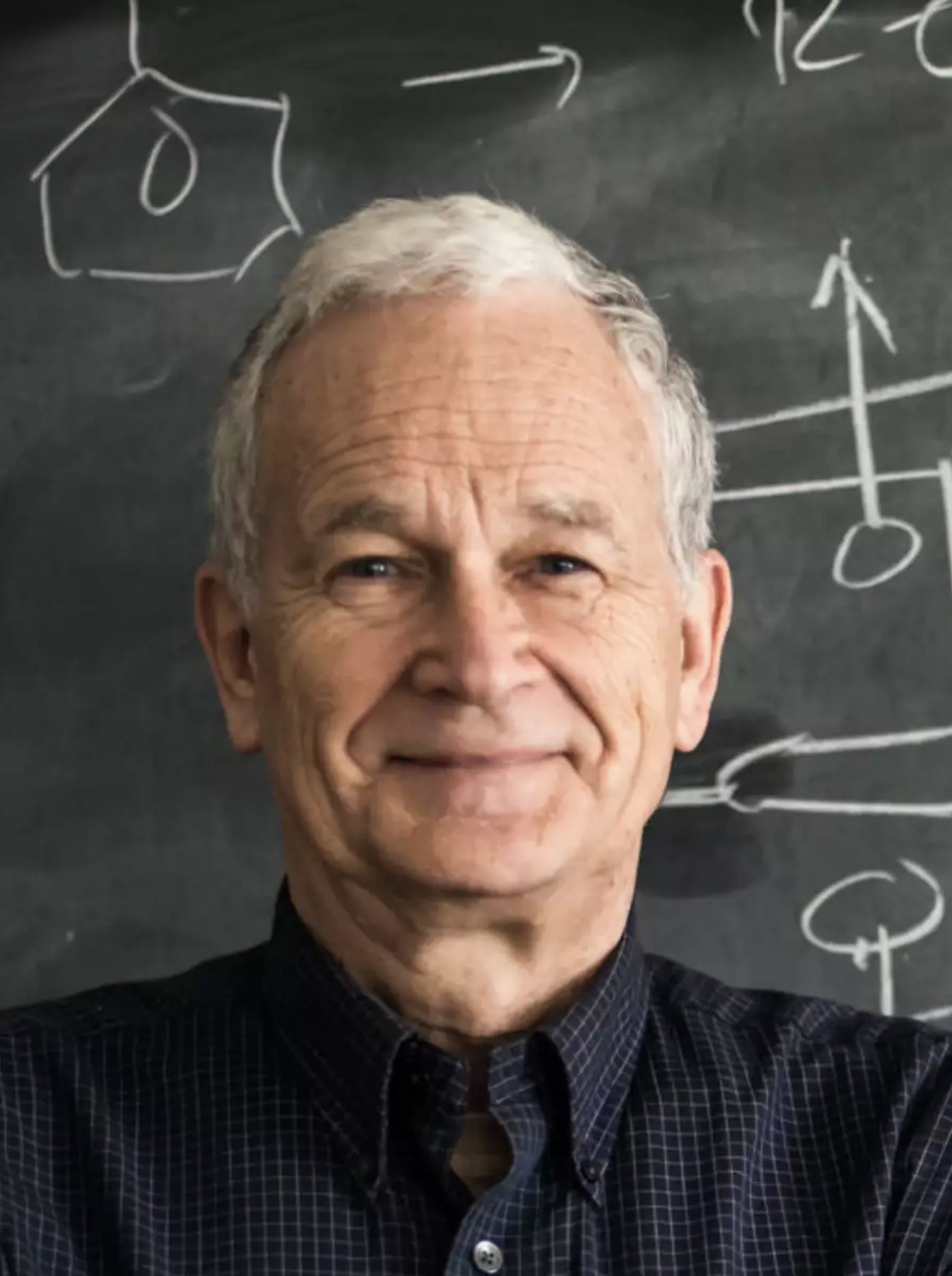 man with white hair in front of a chalk board