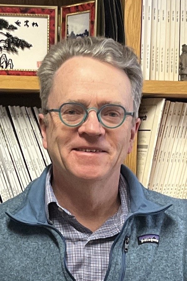 Man with blue glasses standing infront of a bookcase
